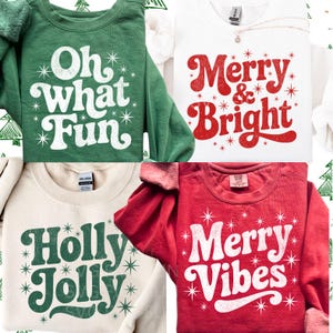 May include: Four sweatshirts with holiday-themed text. The sweatshirts are green, white, beige, and red. The green sweatshirt says "Oh what Fun". The white sweatshirt says "Merry & Bright". The beige sweatshirt says "Holly Jolly". The red sweatshirt says "Merry Vibes".