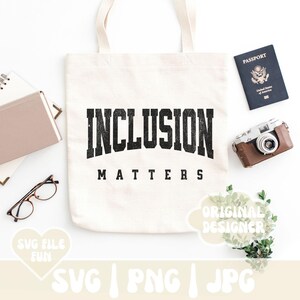 May include: A white tote bag with the text "INCLUSION MATTERS" in black distressed lettering. The bag is on a white surface with a passport, a camera, and a green plant.