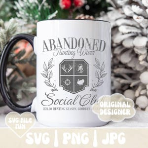 Może przedstawiać: Biały kubek ceramiczny z czarnym uchwytem. Kubek ma graficzny wz&oacute;r z napisem "Abandoned Hunting Wives Social Club" z herbem przedstawiającym symbole związane z polowaniem. Tekst pod herbem brzmi "Hello Hunting Season, Goodbye Jusba."
