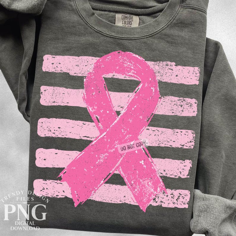 May include: A charcoal gray crewneck sweatshirt featuring a distressed pink ribbon graphic centered over horizontal pink stripes. The graphic includes a small rectangular label with the text DO NOT COPY. The garment has a ribbed collar.