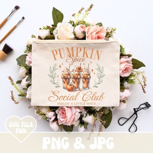 May include: A beige canvas cosmetic bag with the text "Pumpkin Spice Social Club" and an illustration of three pumpkin spice lattes. The bag is surrounded by pink and white roses and greenery. Makeup brushes and an eyelash curler are also visible.