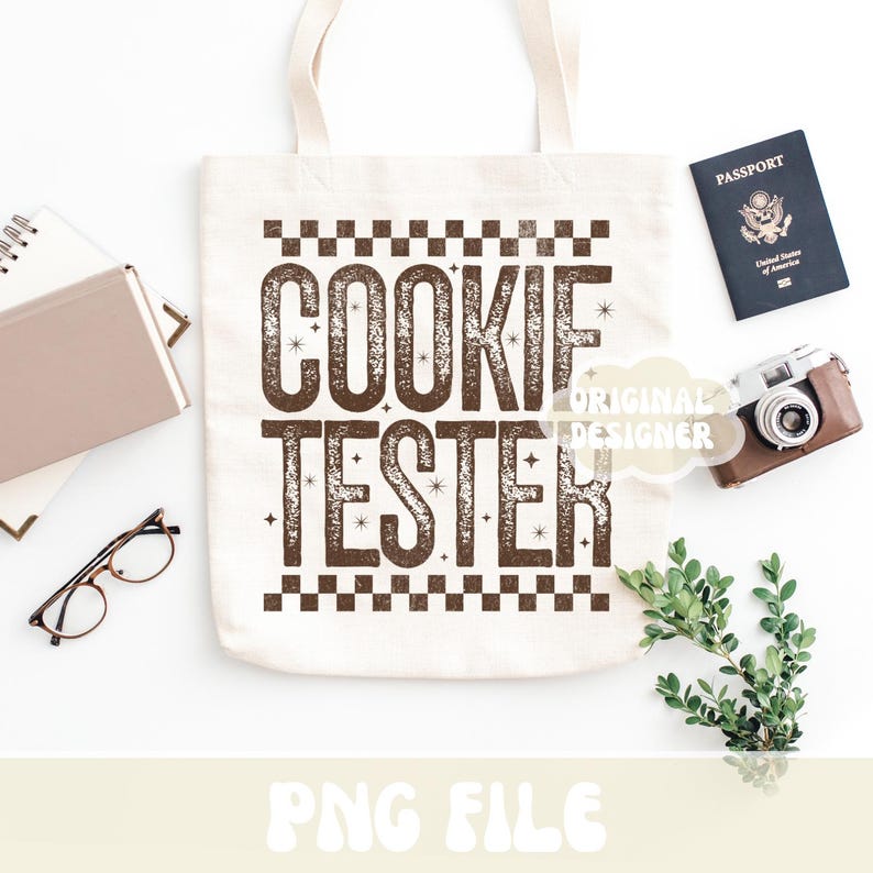 May include: A cream-colored tote bag with the words "COOKIE TESTER" in brown, distressed lettering. The bag is surrounded by a passport, a vintage camera, glasses, and a notebook.