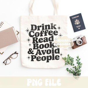 Op de afbeelding: Cr&egrave;mekleurige draagtas met de zwarte tekst "Drink Coffee Read Book & Avoid People". De afbeelding bevat ook een paspoort, een camera, een bril en een klein boek.