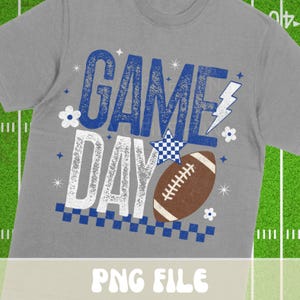 Puede incluir: Una camiseta gris con un dise&ntilde;o de "GAME DAY" en azul y blanco. El dise&ntilde;o incluye un bal&oacute;n de f&uacute;tbol americano, estrellas y un rayo. Es una prenda de vestir informal.