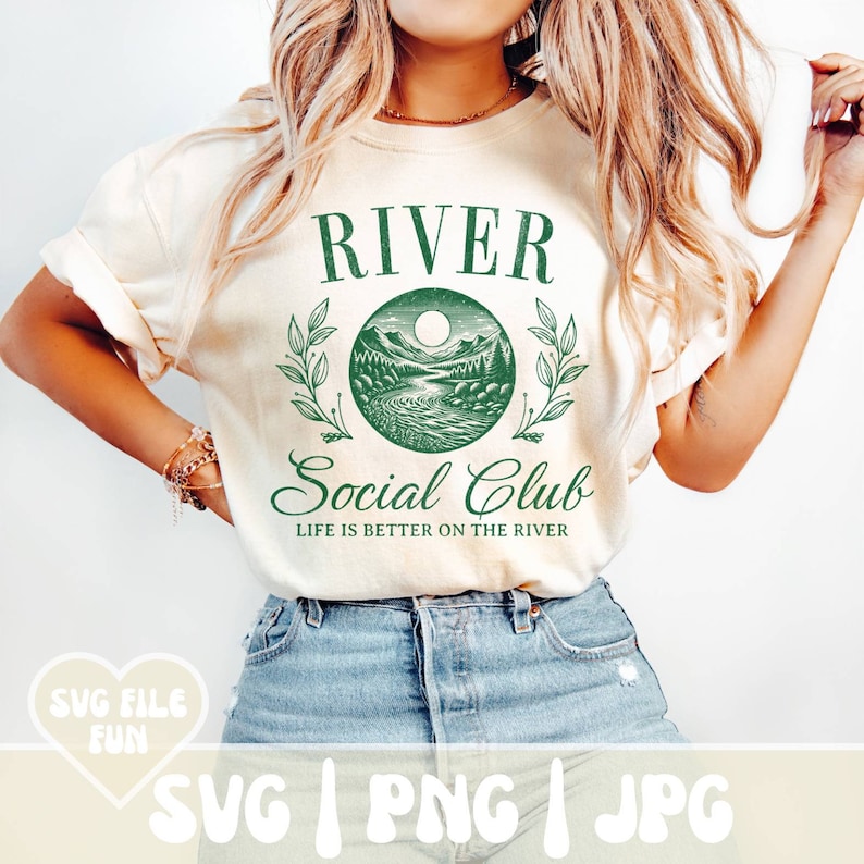 May include: Cream-colored t-shirt with a green graphic that reads "RIVER Social Club" with a scenic river and mountain design. The text "LIFE IS BETTER ON THE RIVER" is below the graphic. The shirt is paired with blue denim shorts.