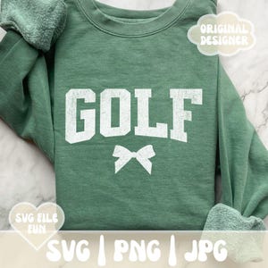 May include: A green sweatshirt with the word "GOLF" in white letters and a white bow underneath. The sweatshirt is on a white and gray marble surface.