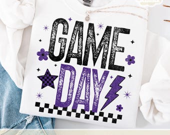 May include: White sweatshirt with the words "GAME DAY" in black and purple, decorated with stars, flowers, and a checkered star. The sweatshirt has a crew neck and long sleeves.