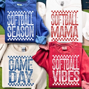 Op de afbeelding: Vier sweatshirts in blauw, wit, crème en rood, elk met een softbalthema. Het blauwe sweatshirt zegt "SOFTBALL SEASON", het witte zegt "SOFTBALL MAMA", het crèmekleurige zegt "GAME DAY" en het rode zegt "SOFTBALL VIBES".