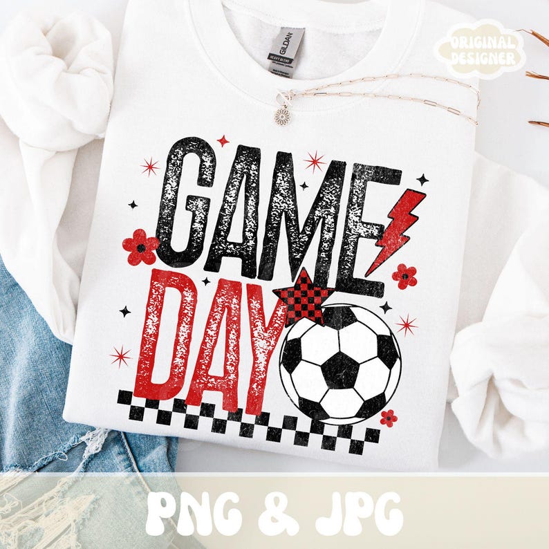 May include: White sweatshirt with the words "GAME DAY" in black and red, along with a soccer ball graphic. The design includes red flowers, stars, and a lightning bolt. The sweatshirt is a Gildan brand.