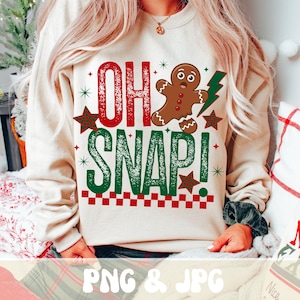 May include: A beige sweatshirt with the text "OH SNAP!" in red and green, along with a gingerbread man graphic and star accents. The design has a festive, holiday theme, perfect for Christmas.