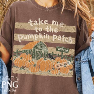 May include: A dark brown short-sleeve t-shirt featuring a graphic print with the text "take me to the pumpkin patch". The design includes a green barn, a "PUMPKINS" sign, a black crow, and multiple orange pumpkins set against a distressed background.