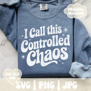 May include: A blue sweatshirt with the text "I Call this Controlled Chaos" in white, retro-style lettering. The design includes starburst accents. The sweatshirt has a crew neck and long sleeves.