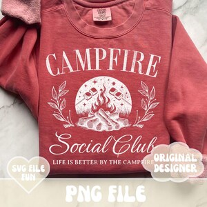 Może przedstawiać: Czerwona bluza z napisem "Campfire Social Club" w kolorze białym. Projekt przedstawia ognisko z piankami na patykach i tekstem "Life is better by the campfire".