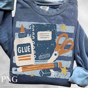 May include: A blue crewneck sweatshirt featuring a graphic print of school supplies including a glue bottle labeled GLUE, a spiral notebook with the text DO NOT COPY, scissors, a pencil, an eraser, and yellow stars on a distressed striped background.