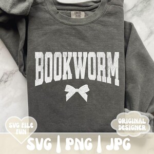 May include: A gray sweatshirt with the text "BOOKWORM" in white letters. A white bow is centered below the text. The sweatshirt is a comfortable, casual style.