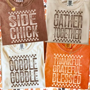 Może przedstawiać: Cztery koszulki Comfort Colors w kolorach brązowym, beżowym, kremowym i pomarańczowym. Każda koszulka ma biały nadruk z napisami: "SIDE CHICK", "GATHER TOGETHER", "GOBBLE GOBBLE" i "THANKFUL GRATEFUL BLESSED".