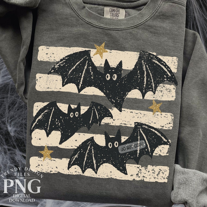May include: A charcoal gray crewneck sweatshirt featuring a graphic print of three black bats flying across horizontal, distressed beige stripes. The design includes small gold stars scattered between the bats. The collar tag reads Comfort Colors.