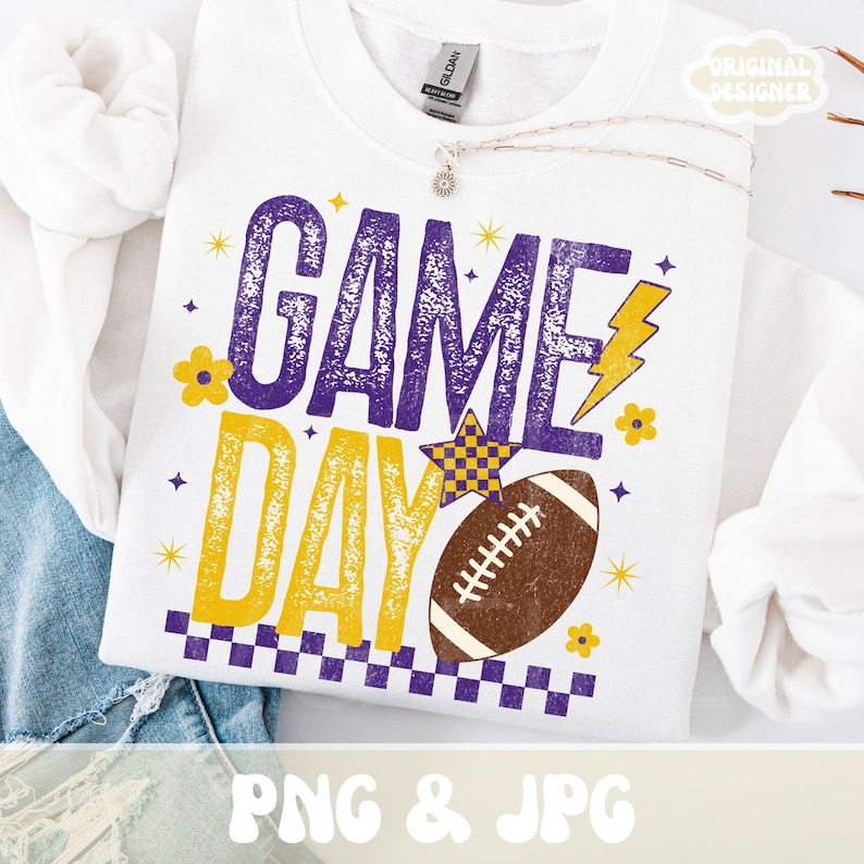 Puede incluir: Sudadera blanca con un gr&aacute;fico "GAME DAY" en morado y amarillo, con un bal&oacute;n de f&uacute;tbol americano, estrellas y un rayo. El dise&ntilde;o incluye un borde a cuadros y detalles florales. Las palabras "PNG & JPG" est&aacute;n en la parte inferior.