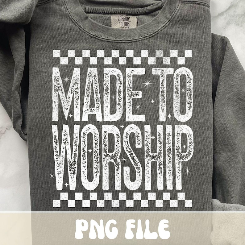 K&ouml;nnte beinhalten: Ein dunkelgraues Sweatshirt mit dem Schriftzug "MADE TO WORSHIP" in gro&szlig;en, verwaschenen wei&szlig;en Buchstaben. Der Text wird von einem Schachbrettmuster umrahmt. Die Marke "Comfort Colors" ist oben sichtbar. Der untere Teil des Bildes zeigt "PNG FILE".