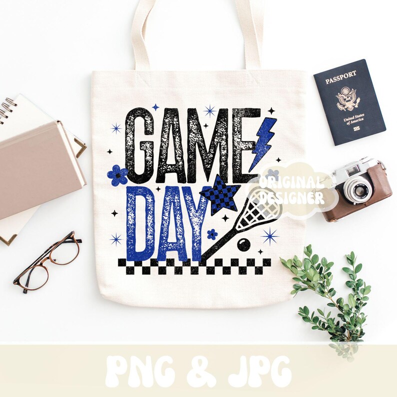 May include: A white tote bag with the words "GAME DAY" in black and blue, along with a lacrosse stick graphic. The bag is surrounded by a passport, camera, glasses, and a notebook.