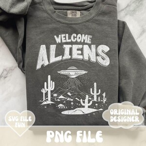 May include: A dark gray sweatshirt with a white graphic design that says "Welcome Aliens" with a UFO and cacti. The graphic is in a vintage style.