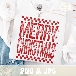 May include: White crew neck sweatshirt with a red "MERRY CHRISTMAS" graphic. The text is in a distressed font, framed by a checkered pattern. The sweatshirt has a "GILDAN" tag. A silver necklace with a pendant is visible.