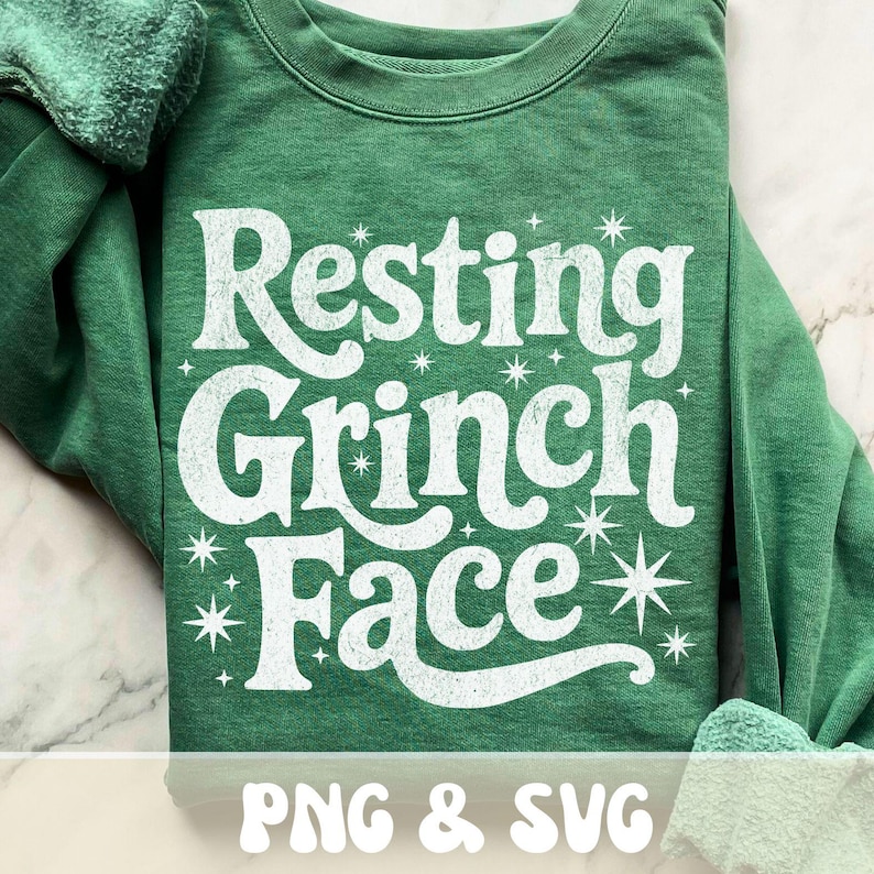 May include: A green sweatshirt with the phrase "Resting Grinch Face" in large, distressed white lettering. The design includes starburst accents. The bottom of the image includes the text "PNG & SVG".