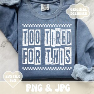 以下が含まれることがあります： 白い文字で「Too Tired For This」と書かれた青いスウェットシャツ。文字は使い古したようなデザインで、チェック柄の縁取りがされている。