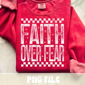 K&ouml;nnte beinhalten: Ein rotes Sweatshirt mit dem Schriftzug "FAITH OVER FEAR" in gro&szlig;en wei&szlig;en Buchstaben. Der Text ist mit kleinen Sternen und einem Schachbrettmuster verziert. Das Sweatshirt hat einen Rundhalsausschnitt und lange &Auml;rmel.