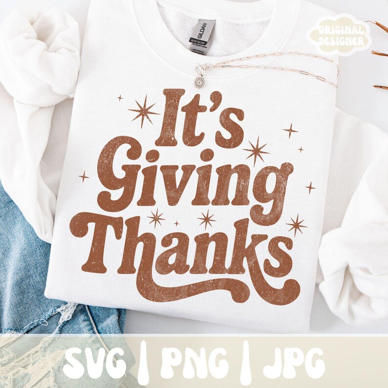 May include: A white sweatshirt with the phrase "It's Giving Thanks" in brown, retro-style lettering. The design includes starburst and star accents. The bottom of the image shows the text "SVG | PNG | JPG". A necklace with a sunburst pendant is visible.