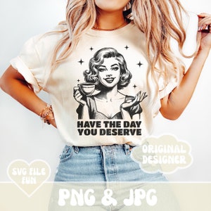 Puede incluir: Camiseta color crema con una ilustraci&oacute;n retro de una mujer sosteniendo una taza de caf&eacute;, con el texto "HAVE THE DAY YOU DESERVE". El dise&ntilde;o incluye estrellas.