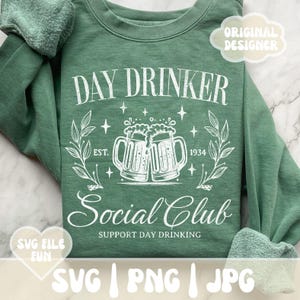 May include: Green sweatshirt with a white graphic design that says "Day Drinker Social Club Est. 1934 Support Day Drinking". The graphic also includes two beer mugs.