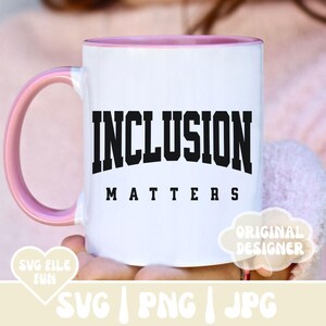 May include: A white ceramic mug with a pink rim and handle. The mug has black text that reads "INCLUSION MATTERS".