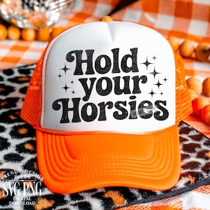 May include: A white and orange trucker hat with the text "Hold your Horsies". The hat has a white front panel, an orange brim, and an orange mesh back. The phrase is in black lettering with star accents. Digital download.