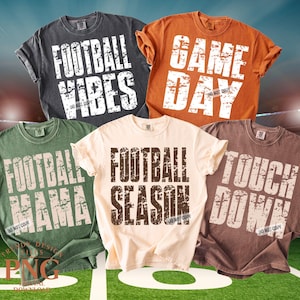 Pode incluir: Cinco camisetas de cores diferentes com frases temáticas de futebol impressas em fontes brancas e marrons desgastadas. As camisetas são em tons de cinza, laranja, verde, creme e marrom. As frases incluem "Football Vibes", "Game Day", "Football Mama", "Football Season" e "Touch Down".