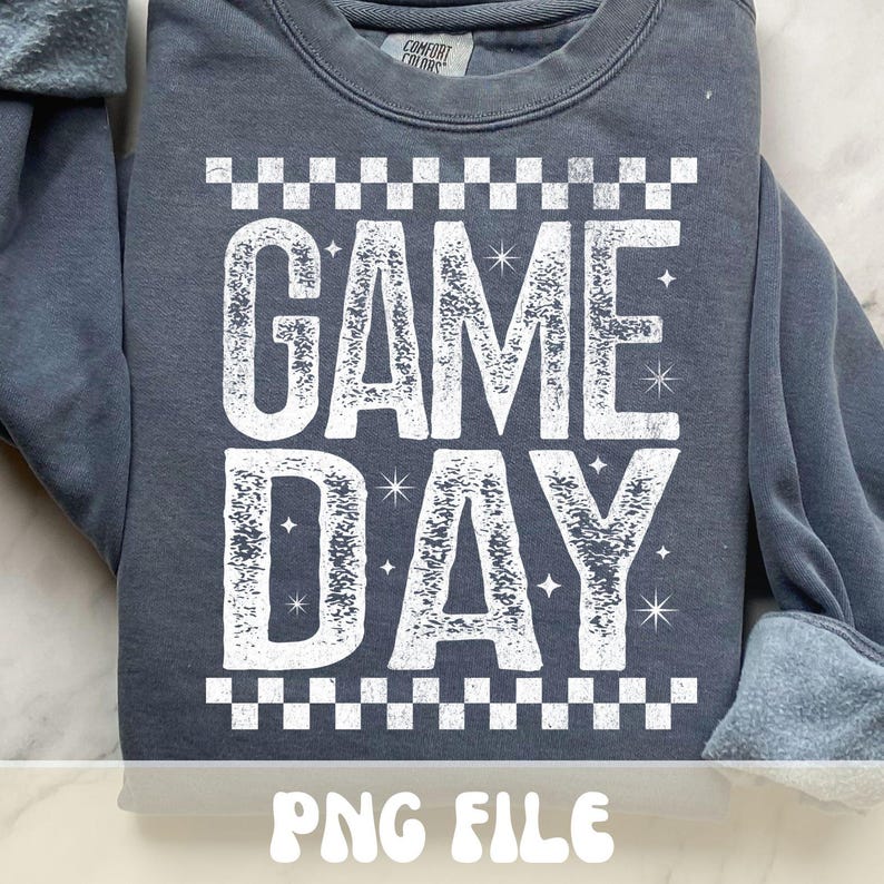 K&ouml;nnte beinhalten: Ein schieferblaues Sweatshirt mit dem Text "GAME DAY" in gro&szlig;en, verwaschenen wei&szlig;en Buchstaben. Der Text wird von einem wei&szlig;en Schachbrettmuster oben und unten eingerahmt. Die Worte "PNG FILE" stehen unten.