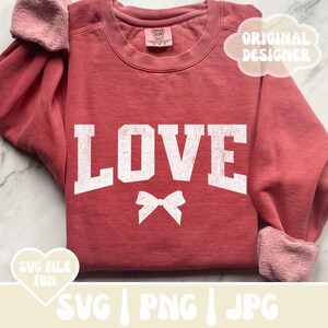 May include: A red sweatshirt with the word "LOVE" in white block letters with a distressed look. A white bow is centered below the word. The sweatshirt has a crew neck and long sleeves.