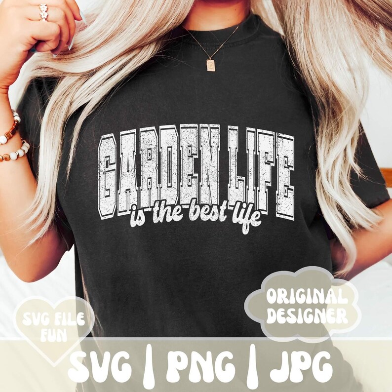 May include: A black t-shirt with white text that reads "GARDEN LIFE is the best life". The text has a distressed, vintage look. The shirt is being worn by a person with long blonde hair.