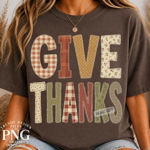 May include: A dark brown short-sleeve t-shirt featuring the text GIVE THANKS in large block letters. Each letter has a unique pattern including orange gingham, solid rust, yellow polka dots, floral prints, and green stripes with a watermark.