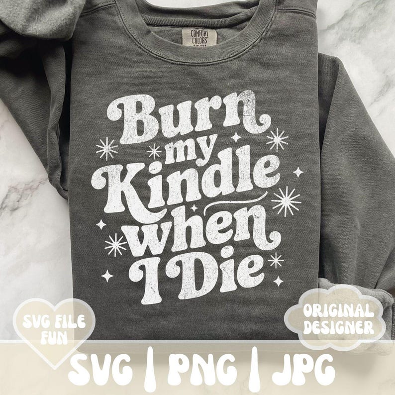 May include: Dark gray sweatshirt with the text "Burn my Kindle when I Die" in white, retro-style lettering. The design includes starburst and star accents. The sweatshirt has a crew neck and long sleeves.