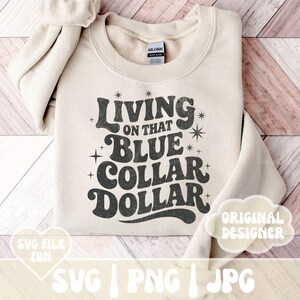 May include: A cream-colored sweatshirt with the text "Living on that Blue Collar Dollar" in a retro font. The design includes star accents. The sweatshirt is folded, with the Gildan brand tag visible. The image also includes SVG, PNG, and JPG file type icons.