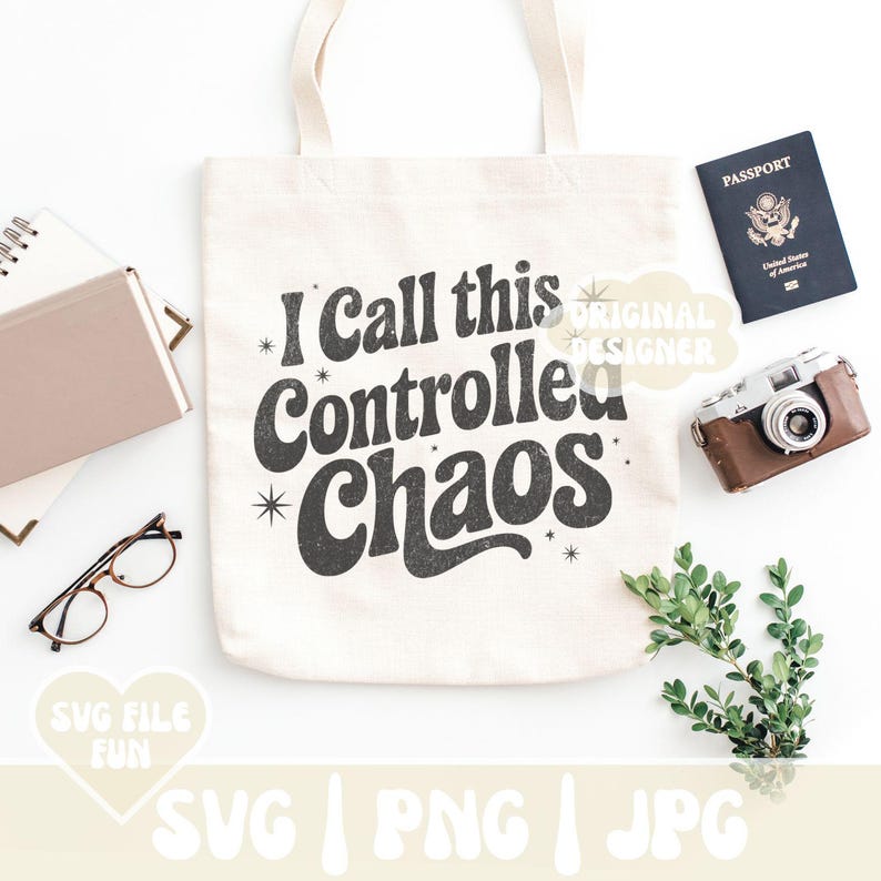 May include: A cream-colored tote bag with the text "I call this Controlled Chaos" in a retro font. The image includes a passport, a vintage camera, glasses, a notebook, and greenery, suggesting a travel or lifestyle theme.