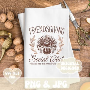 May include: White Friendsgiving Social Club kitchen towel with a brown graphic design. The design includes a pumpkin, wheat, and cutlery. The text reads "FRIENDSGIVING Social Club" and "FRIENDS ARE THE FAMILY WE CHOOSE".