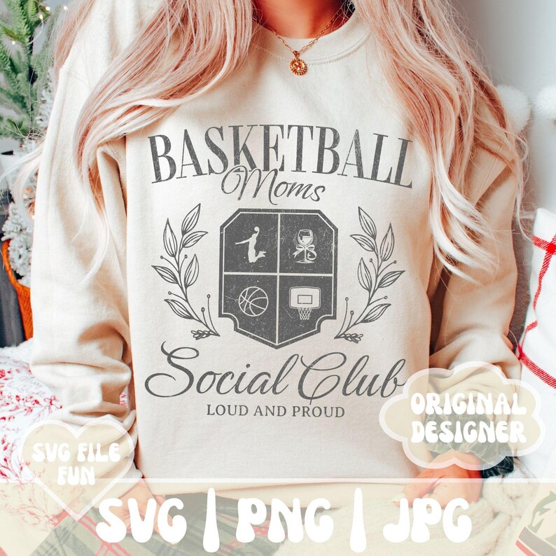 May include: A cream-colored sweatshirt with a graphic design that says "Basketball Moms Social Club Loud and Proud". The graphic features a basketball, a basketball hoop, and a silhouette of a person playing basketball. The text is in a distressed font.