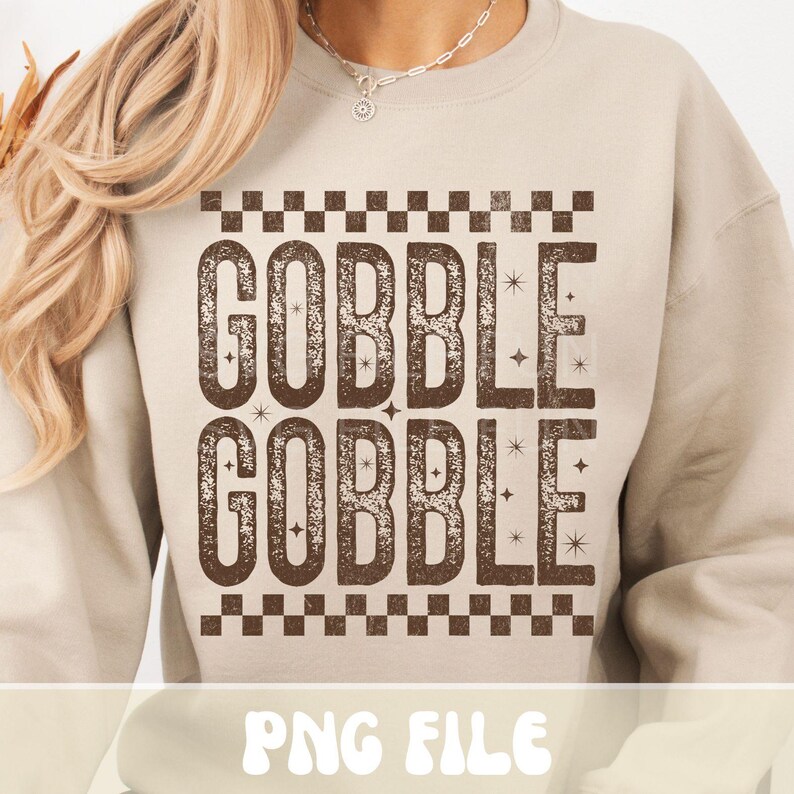 Może przedstawiać: Beżowa bluza z napisem "GOBBLE GOBBLE" w brązowej, postarzanej czcionce. Tekst jest obramowany wzorem w szachownicę. Na dole obrazu widnieje napis "PNG FILE".