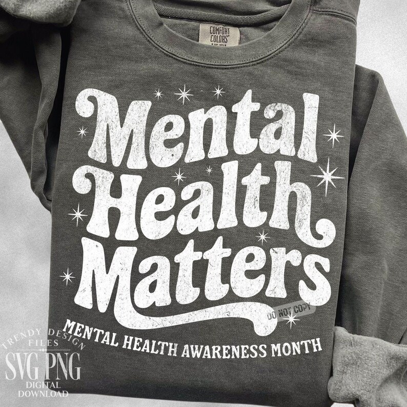 May include: Dark gray sweatshirt with the text "Mental Health Matters" in a distressed white font. The phrase is surrounded by starburst graphics. The bottom of the sweatshirt reads "Mental Health Awareness Month".