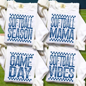 May include: Four white long-sleeved shirts with blue text. The shirts have the phrases "SOFTBALL SEASON", "SOFTBALL MAMA", "GAME DAY", and "SOFTBALL VIBES". Each shirt has a checkered pattern above the text.