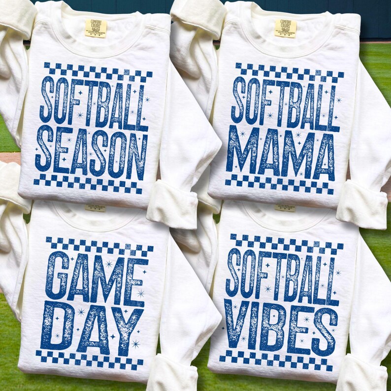 May include: Four white long-sleeved shirts with blue text. The shirts have the phrases "SOFTBALL SEASON", "SOFTBALL MAMA", "GAME DAY", and "SOFTBALL VIBES". Each shirt has a checkered pattern above the text.