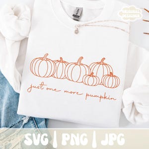 Op de afbeelding: Witte sweatshirt met een oranje pompoenafbeelding. Het ontwerp toont zes pompoenen en de tekst "just one more pumpkin". De onderkant van de afbeelding toont "SVG | PNG | JPG". Het sweatshirt is van het merk Gildan.