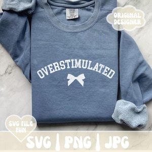 May include: A blue sweatshirt with the text "OVERStimulated" in white with a white bow underneath. The sweatshirt is folded and laid on a white surface.